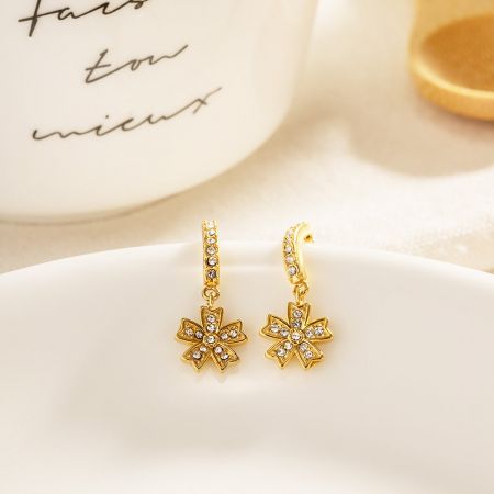 Ein Paar goldene Ohrringe mit Blumenanhängern und Zirkon-Details.