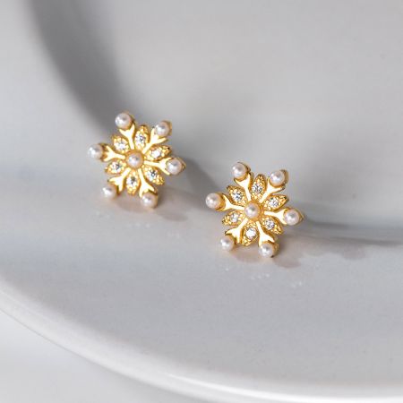 Close-up van de gouden bloemvormige stud oorbellen met een centrale parel, die de ingewikkelde edelsteen details toont.