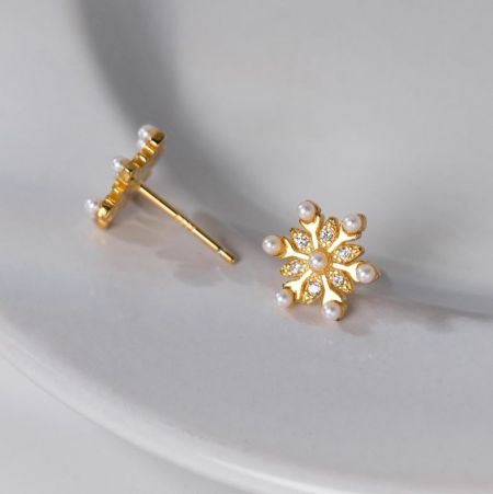 Un paio di orecchini a forma di fiocco di neve con finitura dorata, perle centrali e dettagli di gemme scintillanti.