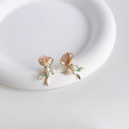白いプラットフォームに展示されたエナメルのバラの花のイヤリングで、ピンクと金の色合いを強調。