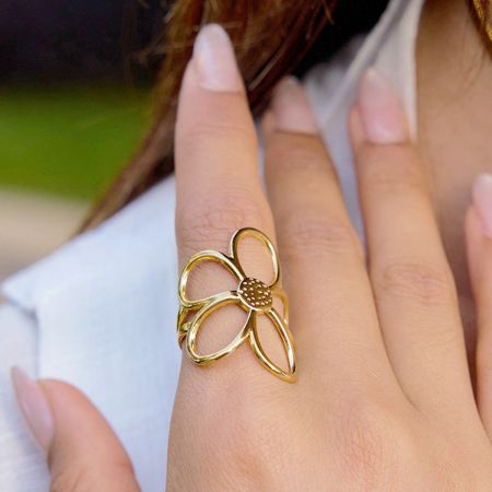 Primer plano del anillo abierto en forma de margarita dorado usado en un dedo, destacando su estilo minimalista inspirado en Corea.