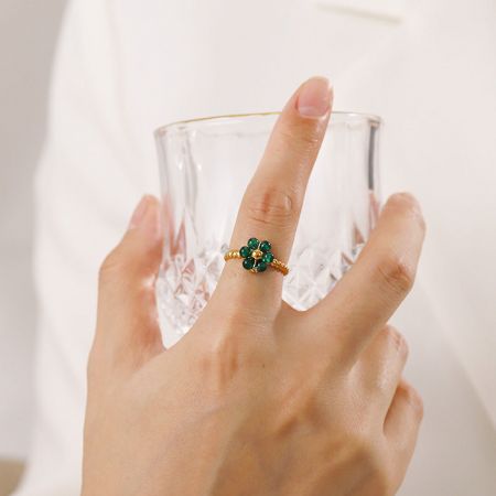 Detalj av ringen med fyrklöverdesign och gröna ädelstenar.