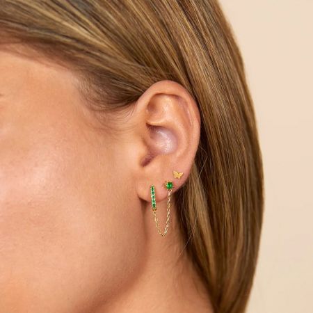 Gedetailleerd uitzicht op drie oorbellen uit de set: een gouden hoop met groene stenen, een kettingoorbel en een vlinder stud.