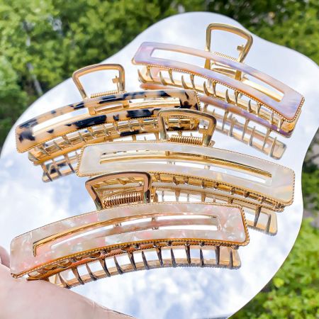Un assortimento di clip per capelli in acetato e metallo dorato esposte su uno sfondo neutro.