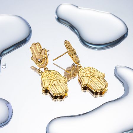 Pendientes colgantes de mano Hamsa Fatima chapados en oro de acero inoxidable (5 pares) - Un par de pendientes colgantes de mano Hamsa Fatima chapados en oro de acero inoxidable, con detalles intrincados y un motivo de ojo central, exhibidos sobre una superficie blanca limpia.