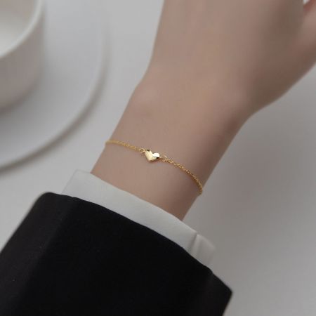 Een gouden minimalistische hartarmband weergegeven op de pols van een mannequin om te laten zien hoe deze gedragen wordt.