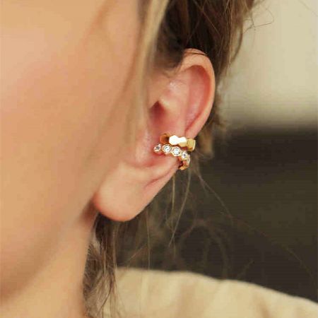 Close-up van een gouden hartvormige oorcuff met diamanten accenten.