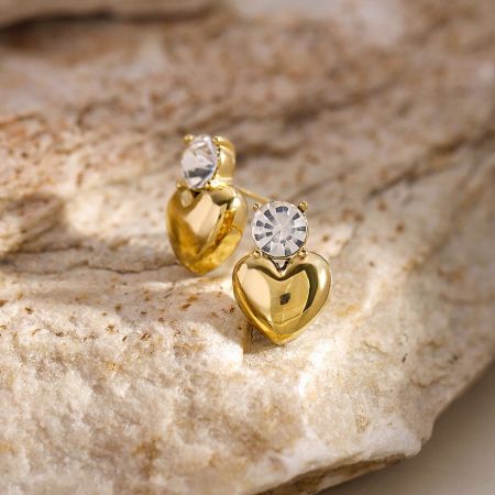 Toma detallada de los pendientes en forma de corazón dorado que muestran el engaste de piedras preciosas claras.
