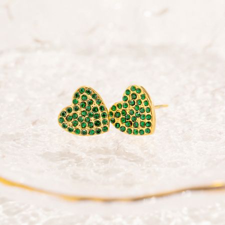 A close-up view of the gold pave green zircon heart stud earrings resting on a white crystal surface.