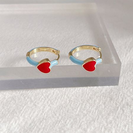 Les boucles d'oreilles en émail rouge et bleu en forme de cœur exposées sur un support en acrylique transparent.