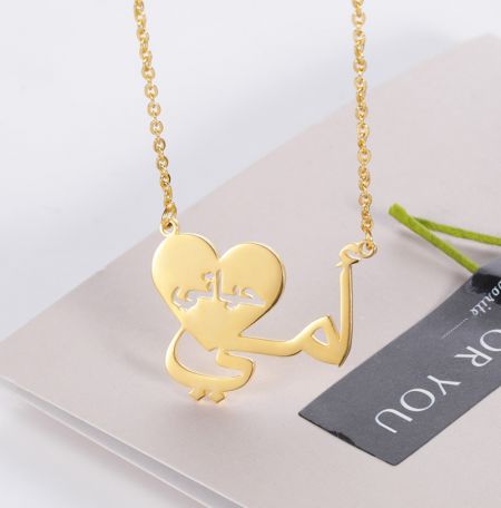 Gros plan sur le collier en or personnalisé en forme de cœur arabe sur une carte d'affichage.