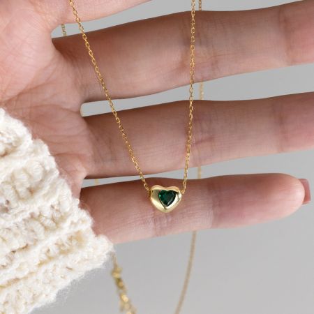 Vista detallada del collar de corazón dorado con un centro de piedra preciosa verde brillante.