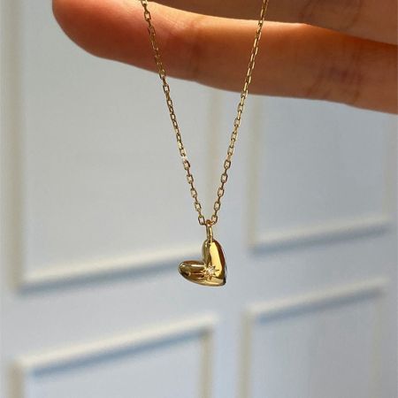 Primer plano del colgante de corazón chapado en oro de 18K con diseño de explosión de estrellas sostenido en la mano para mostrar el detalle.