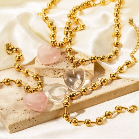 Eine Kollektion von drei Herzanhänger-Halsketten in verschiedenen Farbvarianten, darunter Gold mit rosa und transparentem Quarz.