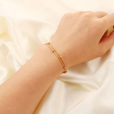 Roestvrijstalen dubbele laag kabelketting kralenarmbanden - Set van 5 - Een close-up van de roestvrijstalen dubbele laag kralenarmband met een hartbedel, gedragen om een pols, die de elegante gouden afwerking toont.