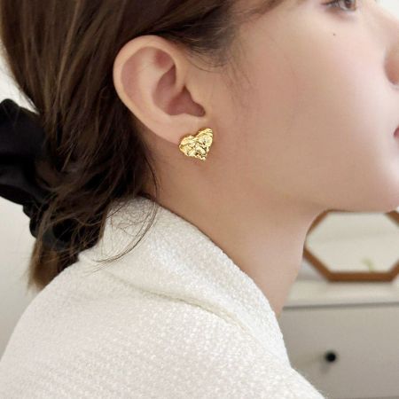 金の不規則なハート型スタッドピアスを着けた女性のクローズアップ。