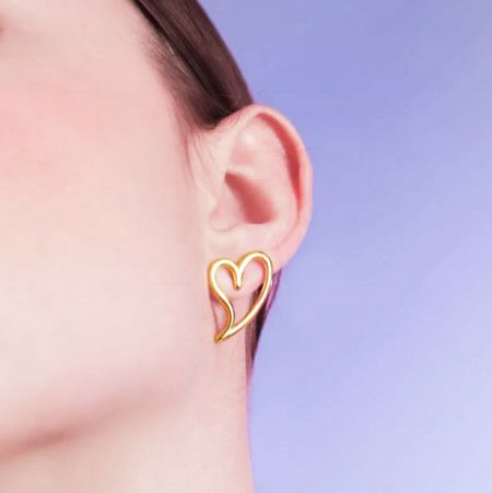 Een model dat de gouden holle hartstud oorbel draagt, die de grootte en hoe het eruitziet in het oor demonstreert.