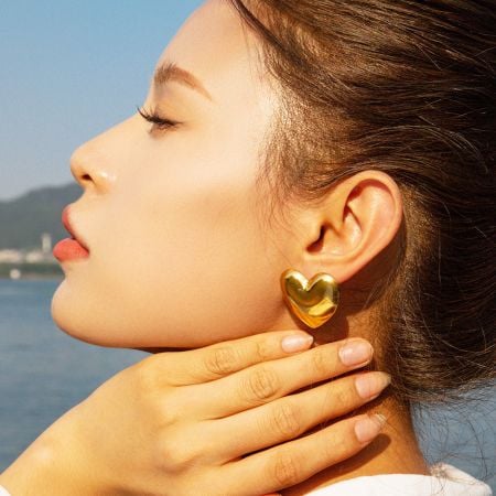 Pendientes de corazón grande gruesos de acero inoxidable hipoalergénico (Juego de 5 pares) - Una vista de perfil en primer plano de una mujer que lleva un pendiente de corazón dorado grueso, mostrando su diseño audaz y acabado pulido.