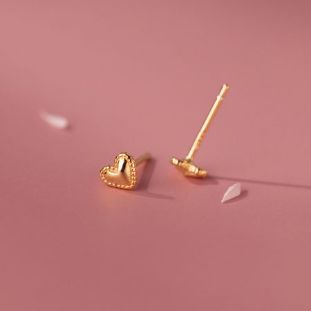 Primo piano di un orecchino a forma di cuore in oro che evidenzia i suoi bordi testurizzati e il tono caldo.