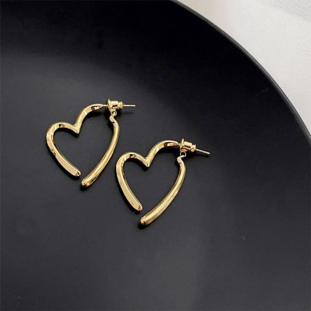 Un par de pendientes minimalistas en forma de corazón dorados sobre un fondo neutro.