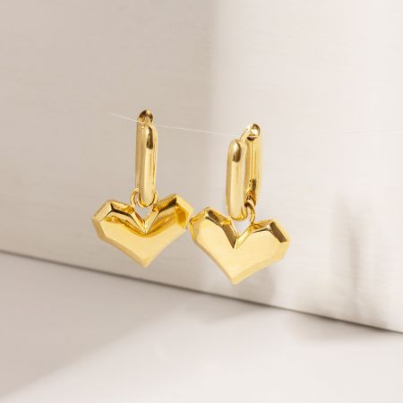 Vista en primer plano de los brillantes pendientes huggie en forma de corazón dorado.