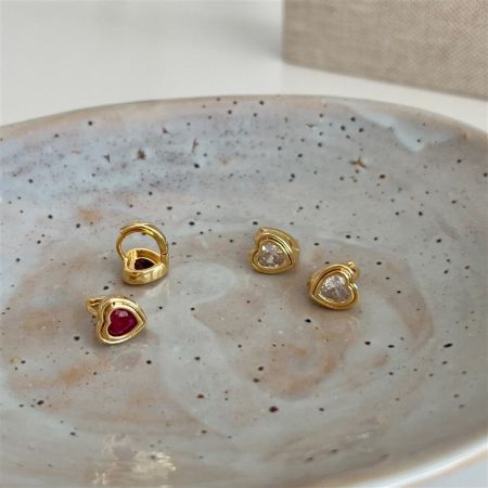 Four pairs of gold heart-shaped huggie earrings displayed on a decorative speckled plate.