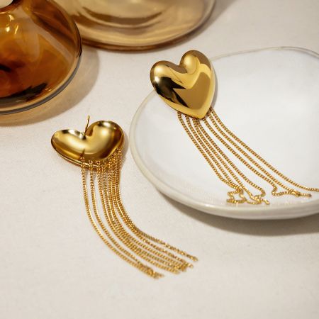 Pendientes de corazón dorado con borlas largas de acero inoxidable. - Un par de pendientes de corazón dorado con borlas largas de acero inoxidable, que presentan un pendiente de corazón dorado pulido con delicadas borlas de cadena colgando abajo, exhibidos sobre un fondo blanco limpio.