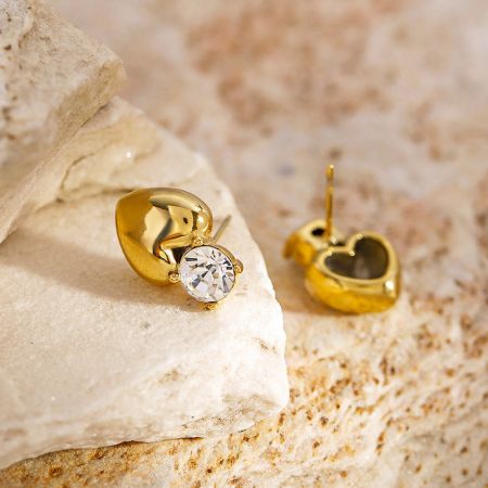 Vista frontal de los pendientes en forma de corazón dorado que destacan las piedras preciosas claras.