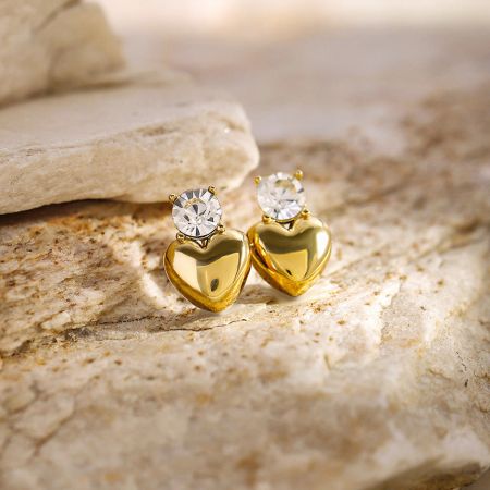 Vista en primer plano del par de pendientes en forma de corazón dorado con piedras preciosas claras.