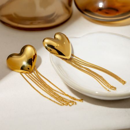 Vista en primer plano del pendiente de corazón dorado con su intrincado detalle de borlas de cadena.