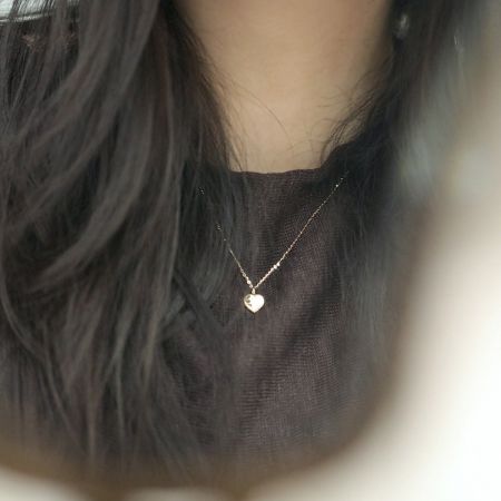 Modelo que lleva el collar con colgante de corazón dorado, destacando su elegante caída y longitud de cadena de 45 cm.
