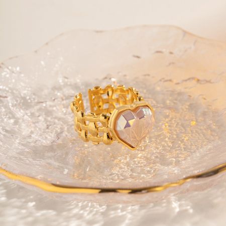 O anel de coração dourado exibido em uma superfície decorativa, destacando seu brilho.