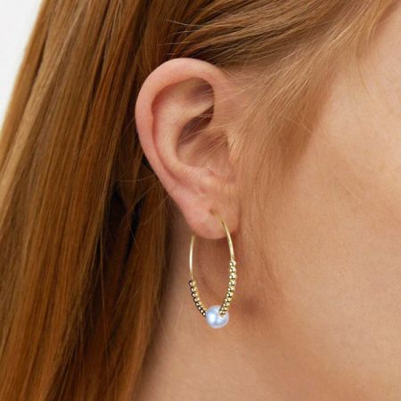 Profilo laterale di un modello che indossa l'orecchino a cerchio con perle d'oro, evidenziando la sua lucentezza e i dettagli.