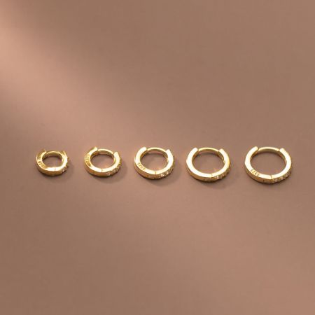 Una collezione di cinque orecchini a cerchio huggie in argento sterling 925 placcati oro con zirconia in varie dimensioni.