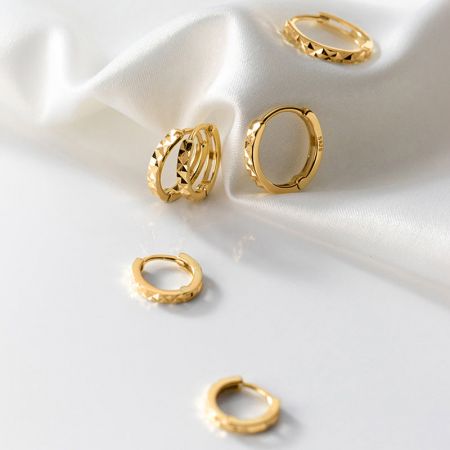Uma coleção estilosa de brincos huggie minimalistas de ouro dispostos sobre uma superfície branca.
