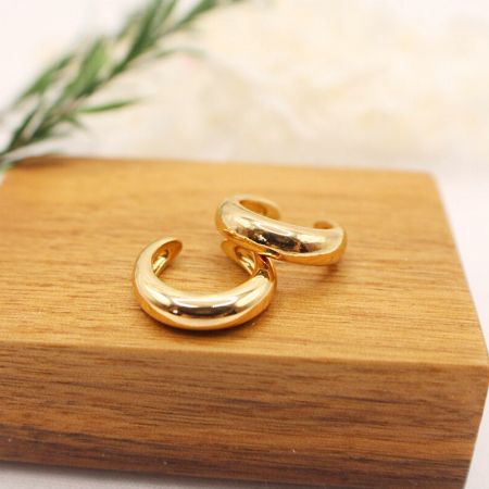 Bracciali auricolari a forma di C in oro su un blocco espositivo in legno.