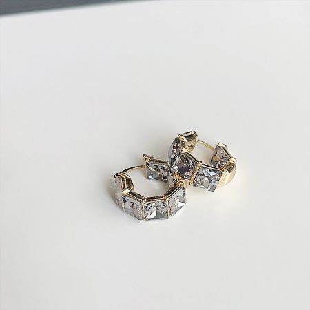 クリアな宝石の六角形パターンの金のフープイヤリングの詳細ショット。