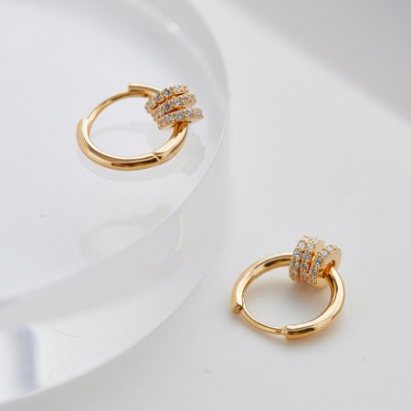 Un par de pendientes de aro de oro con acentos de diamante brillantes sobre un fondo blanco limpio.