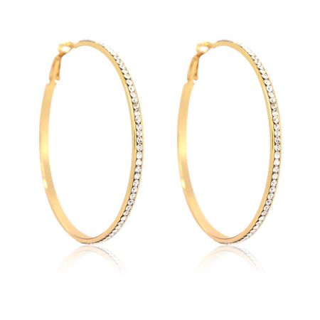 Une paire de grandes boucles d'oreilles en or avec des strass scintillants exposées sur une surface blanche