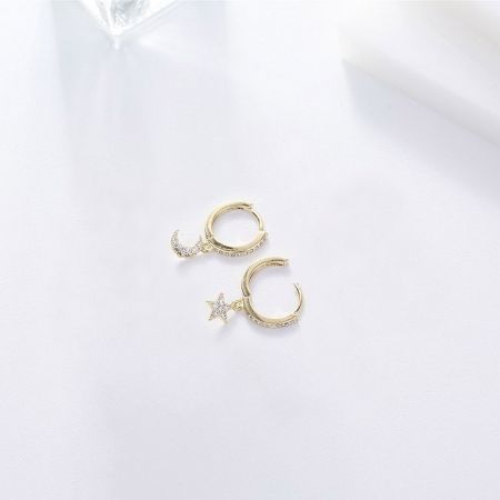 Un autre angle des boucles d'oreilles Huggie sur le thème céleste, montrant les délicates paires de lune et d'étoile.