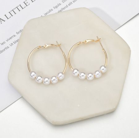 Une vue rapprochée des boucles d'oreilles en perles dorées présentées sur une surface en marbre, mettant en valeur leur texture et leur éclat.