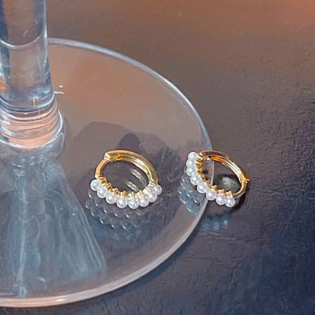 A pair of pearl huggie earrings from the collection displayed on a glass stand.