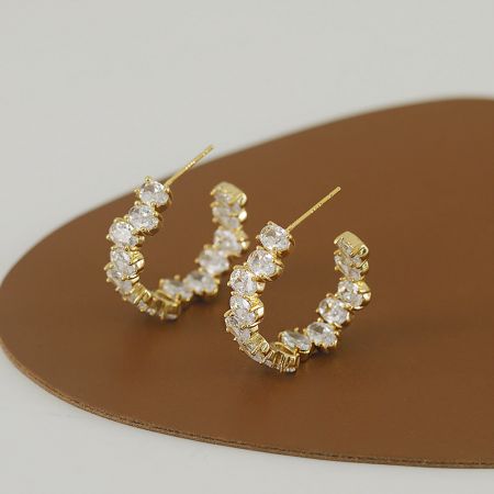 クリアな宝石をあしらった馬蹄型の金のイヤリングで、ユニークなデザインを展示。