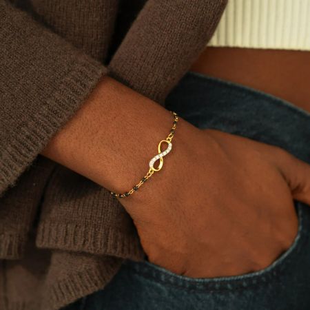 A detailed view of the gold infinity symbol bracelet, emphasizing the brilliant white zircon stones.