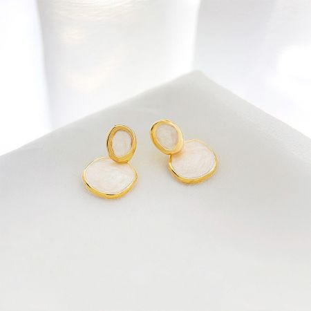 Close-up view of the gold-plated drop earrings, highlighting the iridescent quality of the cream-white enamel.