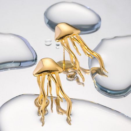 Close-up van de gouden kwal oorbellen op een witte ondergrond met waterdruppels, die hun waterdichte kwaliteit benadrukken.
