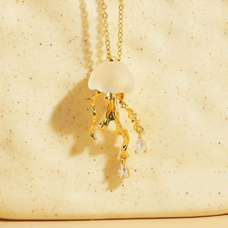 Primo piano dettagliato della collana di medusa in oro, che mostra il cappello bianco e i tentacoli di cristallo scintillanti.