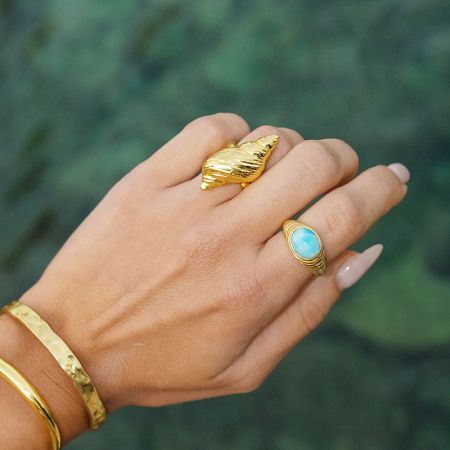 Roestvrijstalen Strandjuwelen Conch Shell Verstelbare Ringen (Set van 5) - De hand van het model toont de goudkleurige roestvrijstalen ringenset met strandthema, inclusief een schelp en turquoise ontwerp.