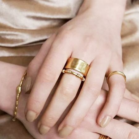 Manos de modelo mostrando múltiples anillos y pulseras de oro de la colección.