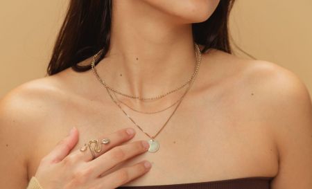 Modello che indossa una collana d'oro a strati e un set di anelli realizzati in acciaio inossidabile placcato in iono, durevole e ipoallergenico.